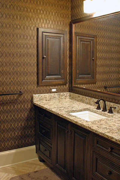 Masculine Bathroom with dark cabinets, stone floor, medicine cabinet and wallpaper.