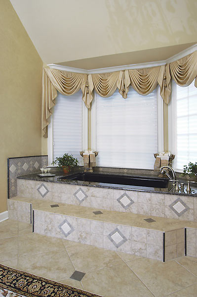 Soaking tub with tiled steps, privacy shades and custom window treatments enhance this master bath